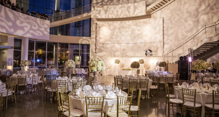 Round dinner tables with white flowers inside the Rotunda at night, with patterned light on the walls